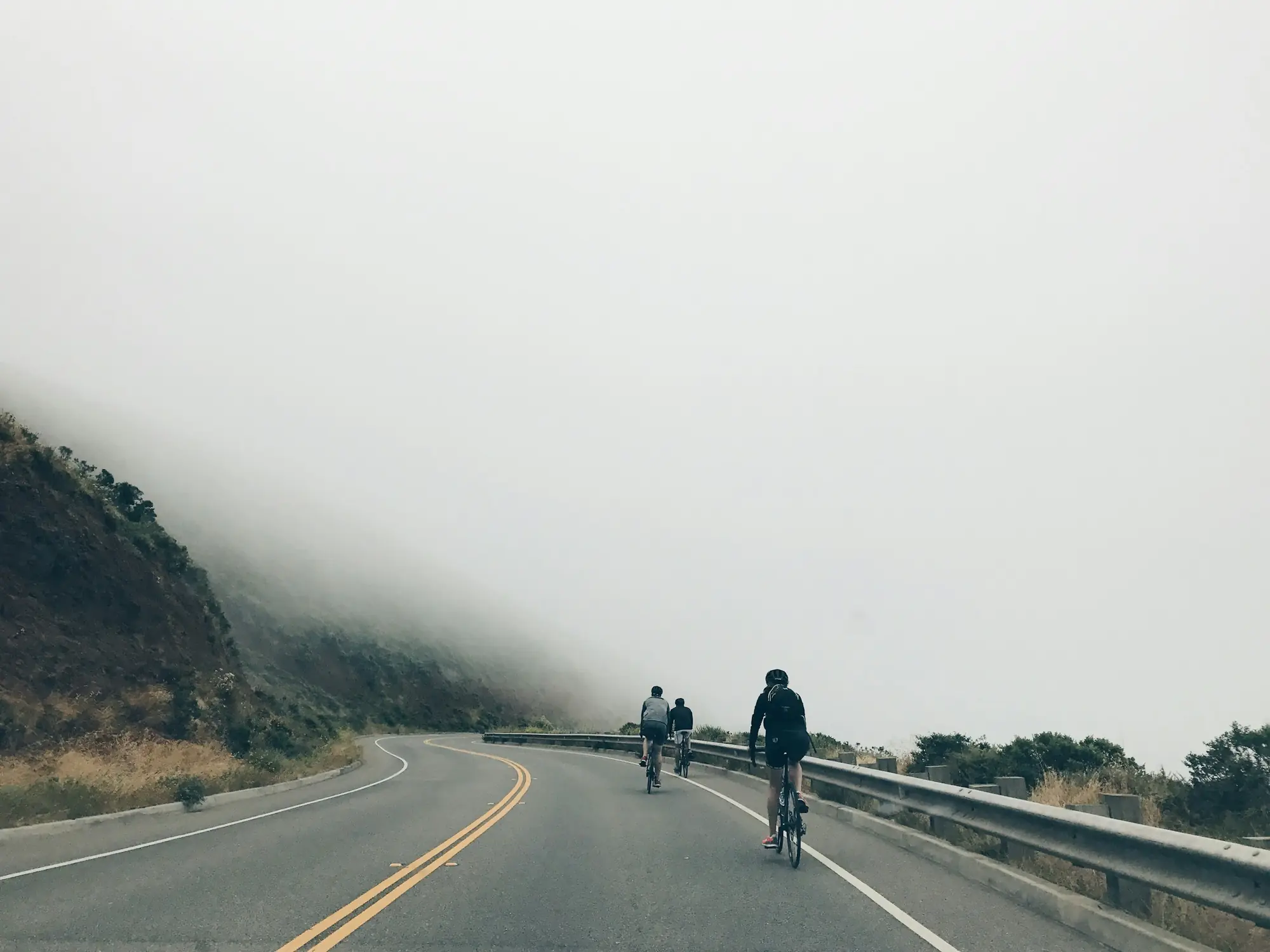 Trois coureurs sur une route de montagne qui se perd dans le brouillard.
